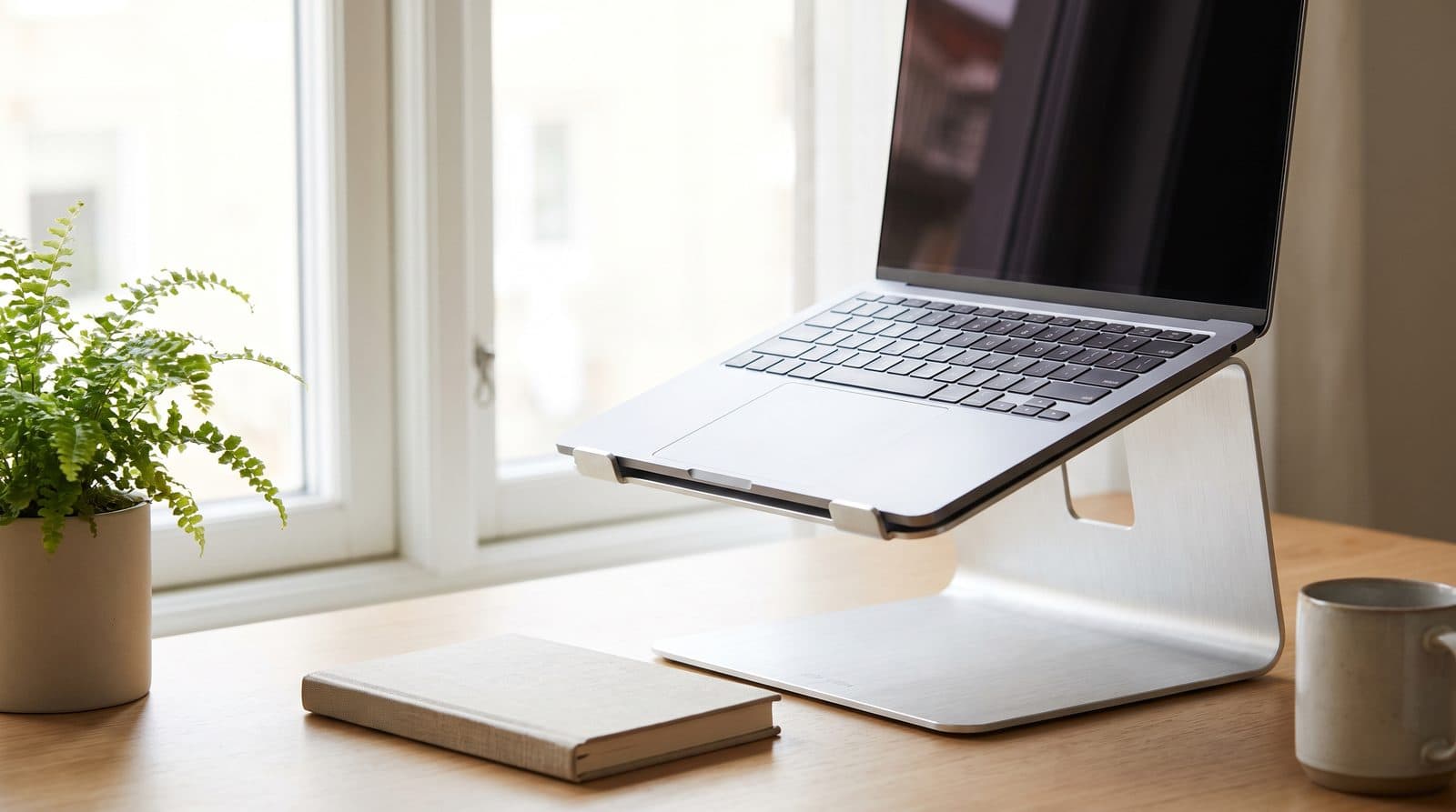 Slim aluminum laptop stand raising a laptop on a small desk in a bright home office