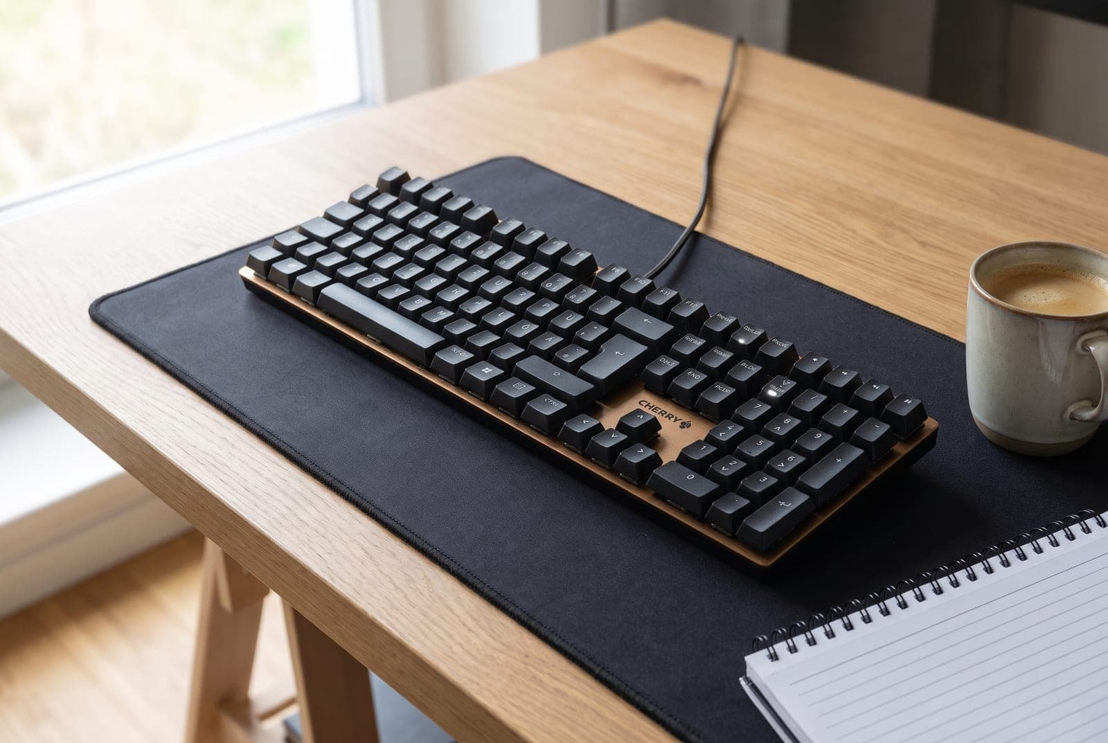 Cherry KC 200 MX full-size mechanical keyboard in black and bronze on a home-office desk, its brushed aluminum top plate catching soft daylight