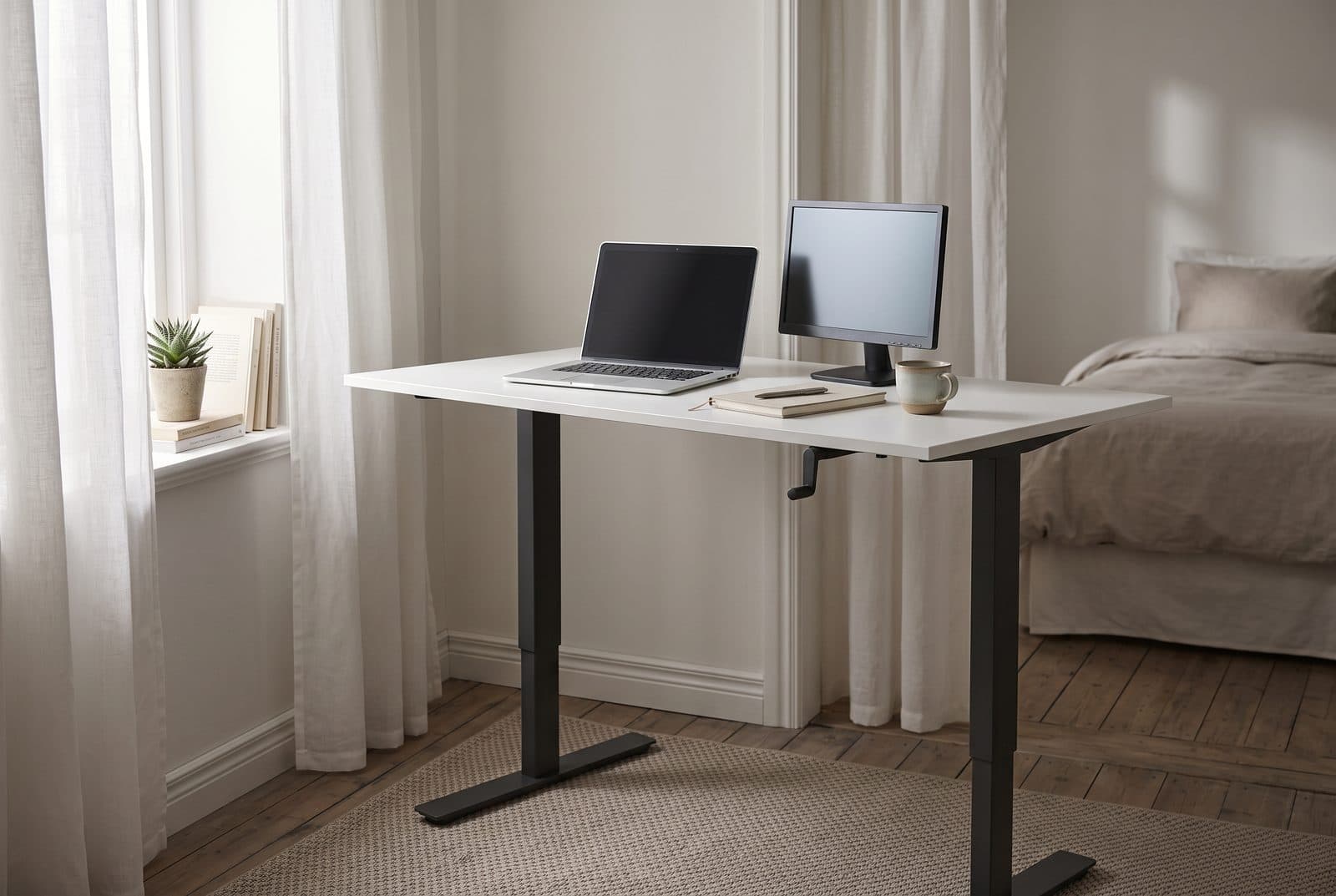 IKEA Trotten crank standing desk with a white top and anthracite legs raised to standing height in a bedroom corner with no power cord in sight