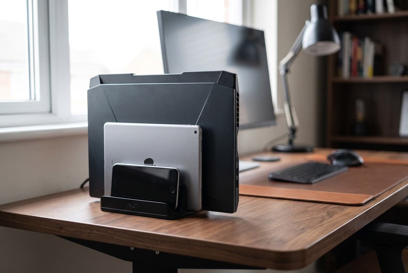 JARLINK black aluminum dual-slot vertical stand holding a thick gaming laptop and a tablet upright on a desk