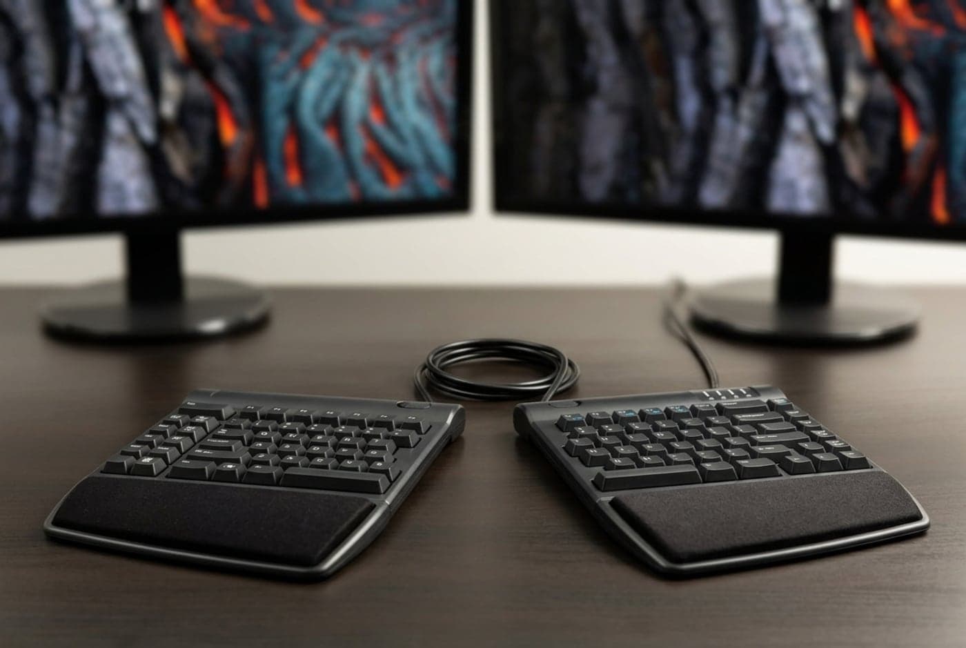 Kinesis Freestyle2 split ergonomic keyboard with its two black halves separated on a desk, connected by a short linking cable, standard key layout
